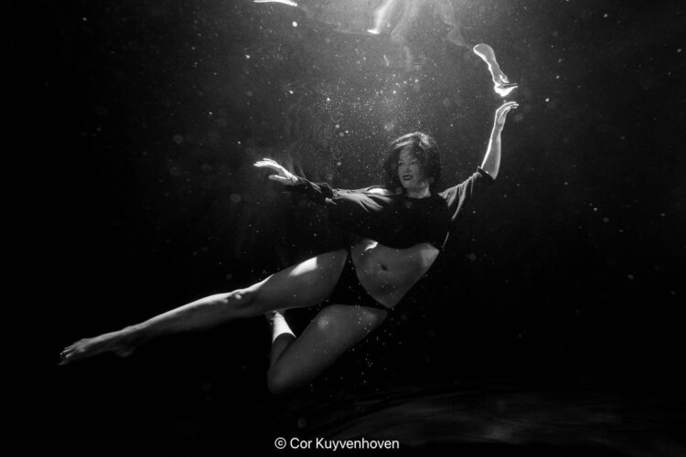 Een prachtige artistieke zwart-wit onderwaterfoto van een vrouw in beweging, met creatieve belichting en waterbubbels, perfect voor kunst- en fotografie doelen.