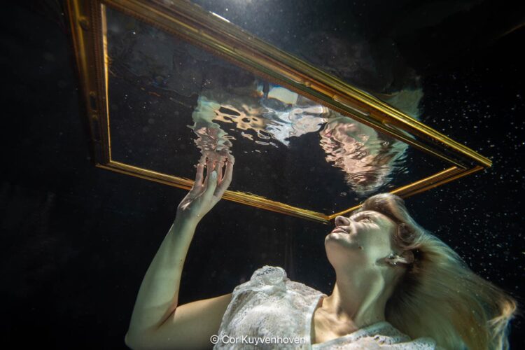 Een vrouw onderwater met spiegel en gouden lijst, symboliseert creativiteit en kunstzinnigheid, vastgelegd door Cor Kuyvenhoven voor inspirerende kunst- en lifestylebeelden.