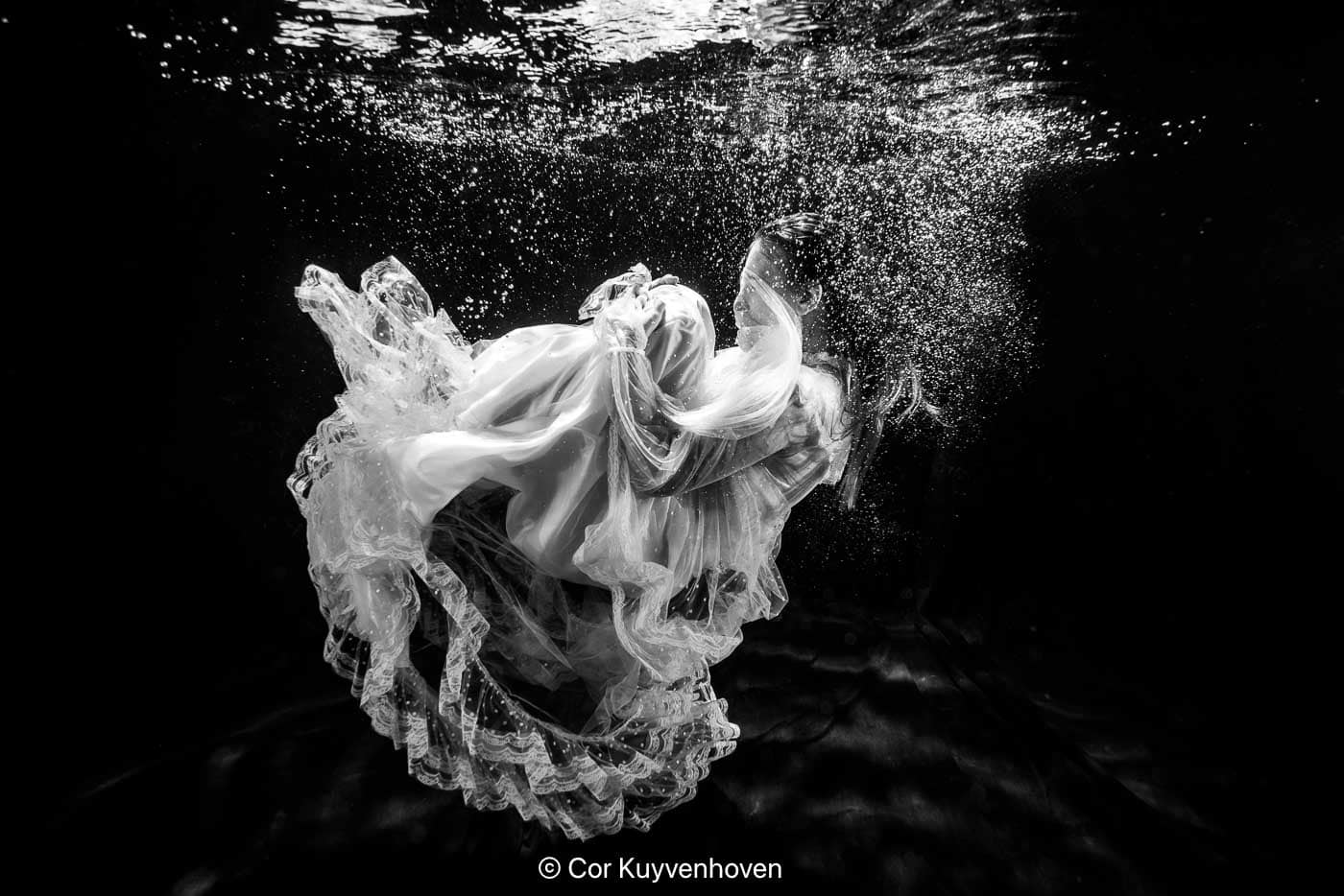 Kunstvolle foto van een vrouw in een jurk onder water met zwevende stof en bubbels, creatief en artistiek, geschikt voor fotografie, mode en kunstliefhebbers.